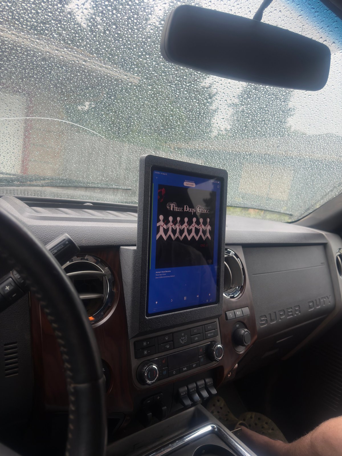 Car interior with touchscreen infotainment system displaying a retro video game, frosted windshield visible above dashboard