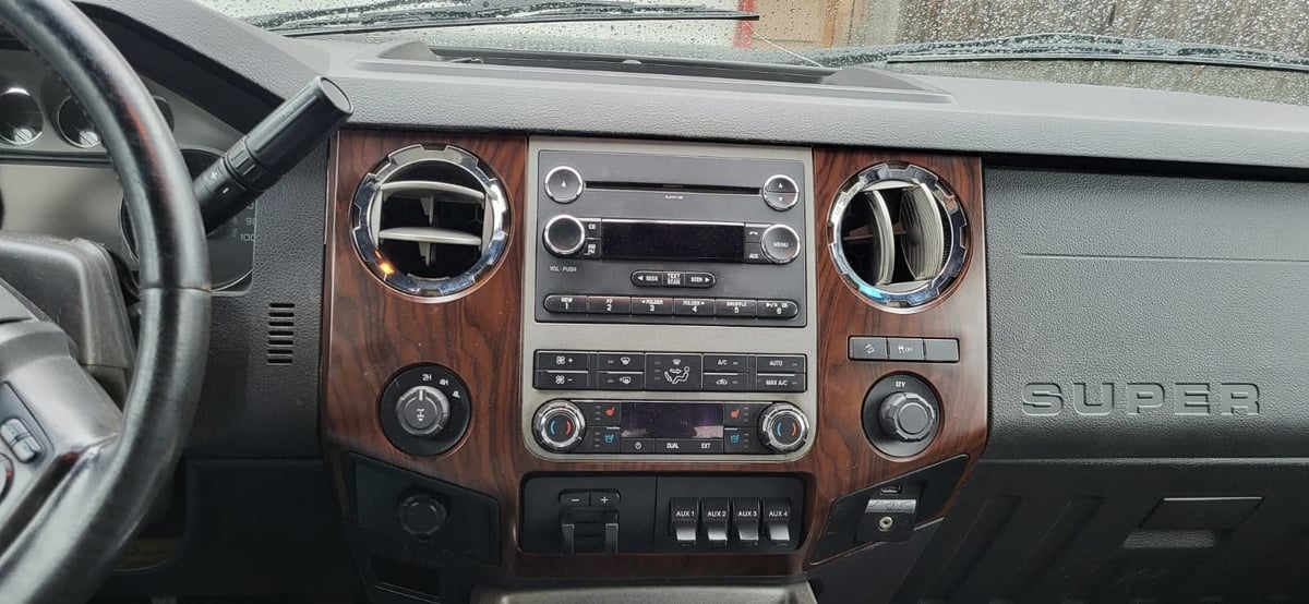 Interior dashboard of a Ford Super Duty truck with wood trim, showing steering wheel, climate controls, audio system, and gauge cluster